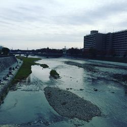 City by river against cloudy sky