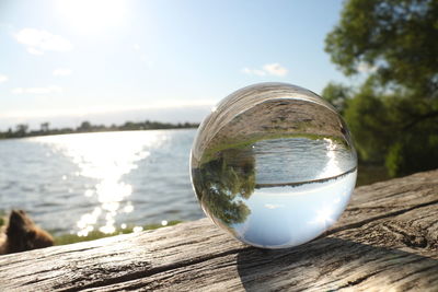 Close-up of crystal ball on wooden table by lake against sky
