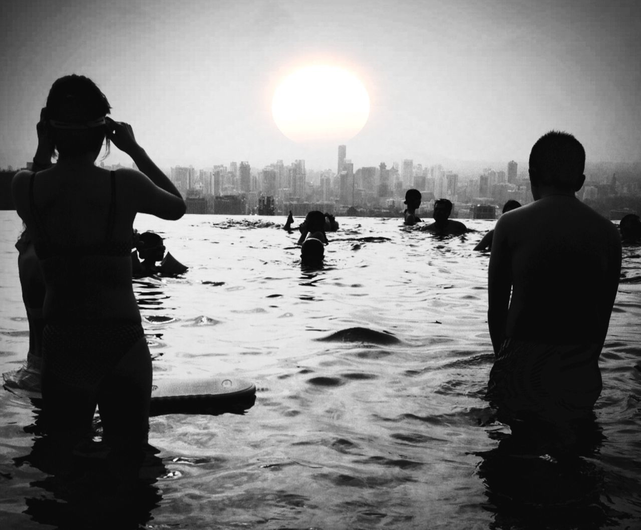 water, silhouette, men, lifestyles, leisure activity, standing, waterfront, sea, togetherness, rear view, reflection, bonding, clear sky, person, river, built structure, sun, love