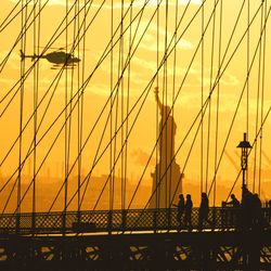 Suspension bridge in city against sky during sunset