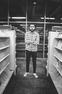 Portrait of young man standing amidst shelves in store