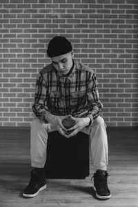 Full length of young man sitting against wall