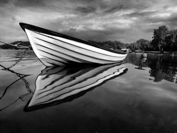 Boat moored on lake against cloudy sky