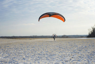 Young man motor paragliding over field against sky