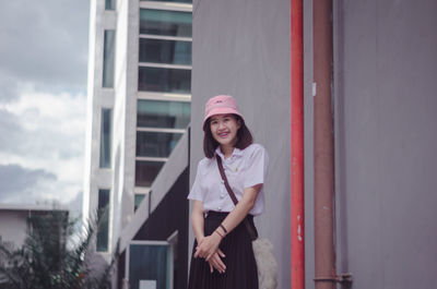 Portrait of smiling young woman standing against building