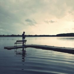 Silhouette man standing on lake against sky during sunset