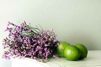 Close-up of limes with bunch of flowers on table