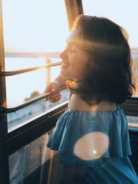 Side view of young woman enjoying sunlight while standing at window