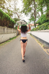 Rear view of woman carrying surfboard on road