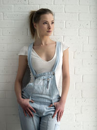 Beautiful woman in bib overalls standing against white wall