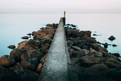 Rocks on beach against sky. pier stretching out in a calm sea. long exposure 