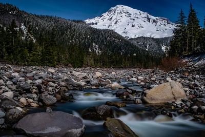 Scenic view of stream by snowcapped mountains against sky