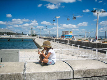 Full length of man sitting on bridge against sky