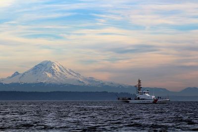 Boat sailing in river against mt rainier and cloudy sky at dusk