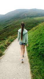 Rear view of teenage girl walking on pathway towards mountain