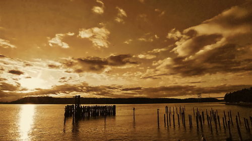 Silhouette wooden posts in lake against sky during sunset