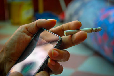 Photo of hands seen holding mobile phones and cigarettes