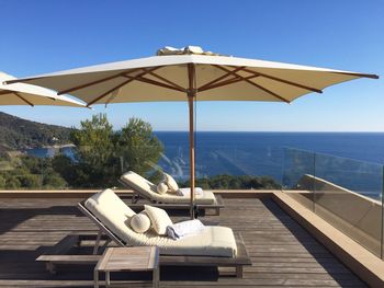 Deck chairs by sea against clear blue sky