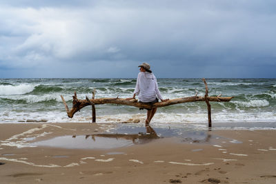 Rear view of woman standing at beach against sky