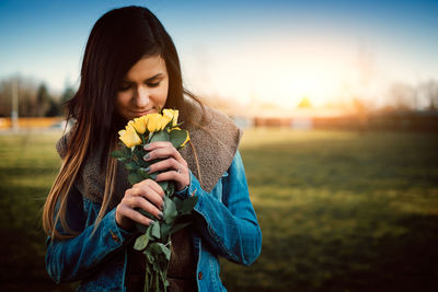 Smiling young woman smelling roses while standing on field