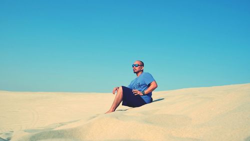 Full length of young man sitting on sand