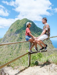 Side view of woman sitting on railing against sky