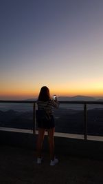 Rear view of woman looking at sea against sky during sunset