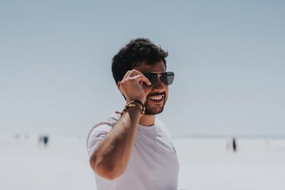 Smiling young man wearing sunglasses standing against clear sky during sunny day