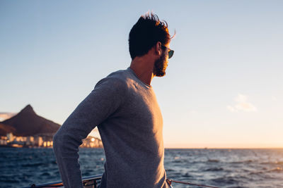 Young man standing in boat on sea against sky