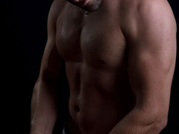 Midsection of shirtless man against black background