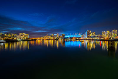 Illuminated city by sea against sky at night