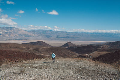 Rear view of man walking on mountain against sky