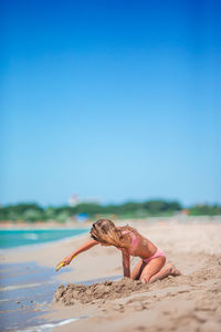 Side view of woman sitting on beach against clear blue sky