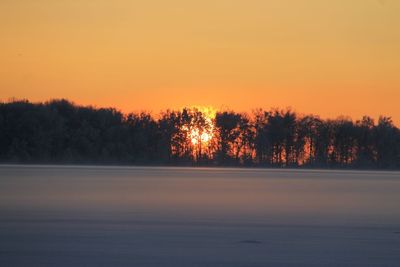Silhouette trees by lake against sky during sunset