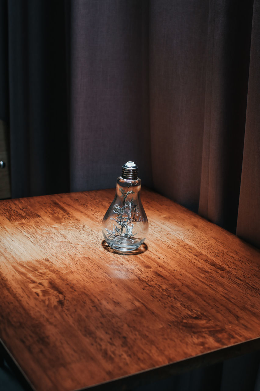 CLOSE-UP OF EMPTY GLASS BOTTLE ON TABLE AGAINST WALL