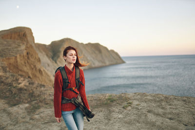 Portrait of young woman standing on beach against sky