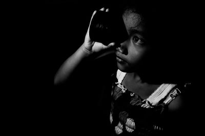Close-up of girl looking through lens against black background