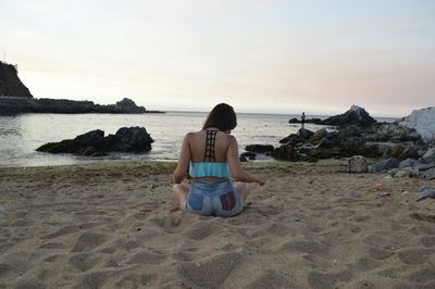 Woman sitting on rock at beach against sky