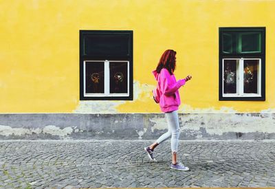 Side view full length of woman walking by building on footpath