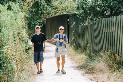 Full length of man and woman walking on footpath by plants