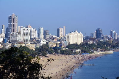 Cityscape by sea against clear blue sky
