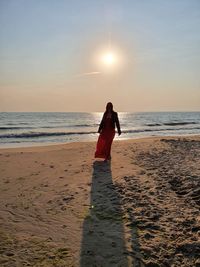 Rear view of woman on beach against sky during sunset