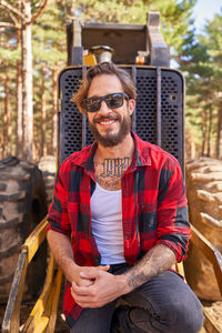 Portrait of young tattoed man leaning on against an excavator