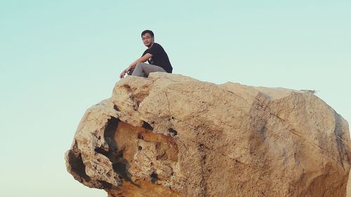 Low angle view of young woman standing on cliff against clear sky