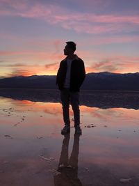 Man standing on beach against sky during sunset