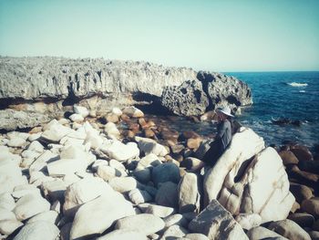 Rocks by sea against clear sky
