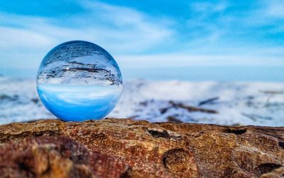 Close-up of crystal ball on beach against blue sky