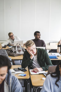 Thoughtful young man sitting with hand on chin in classroom