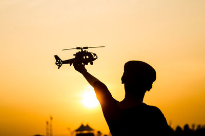 Silhouette boy playing on helicopter against orange sky during sunset