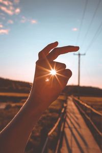 Optical illusion of cropped hand holding sun against sky during sunset